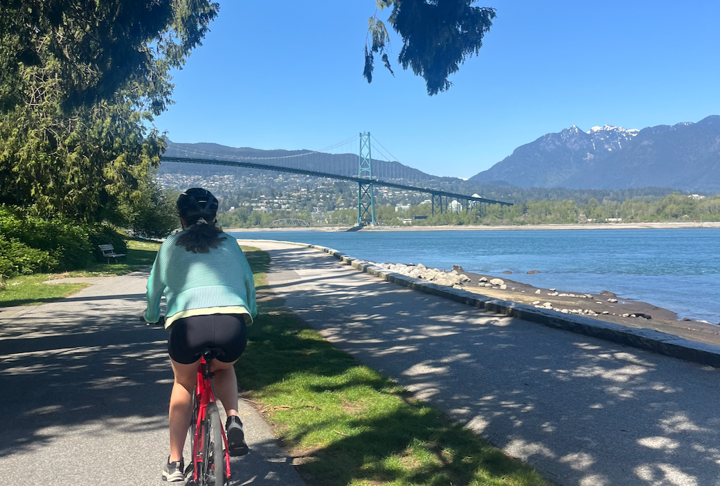 Nuala riding a bike with water to the right and a bridge in the distance