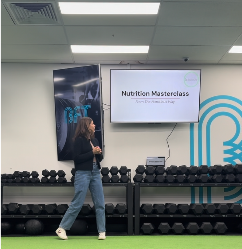 Person walking past a screen displaying 'Nutrition Masterclass' in a gym setting.