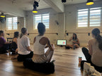 Group of people in a yoga studio with a screen displaying content and Nuala presenting.
