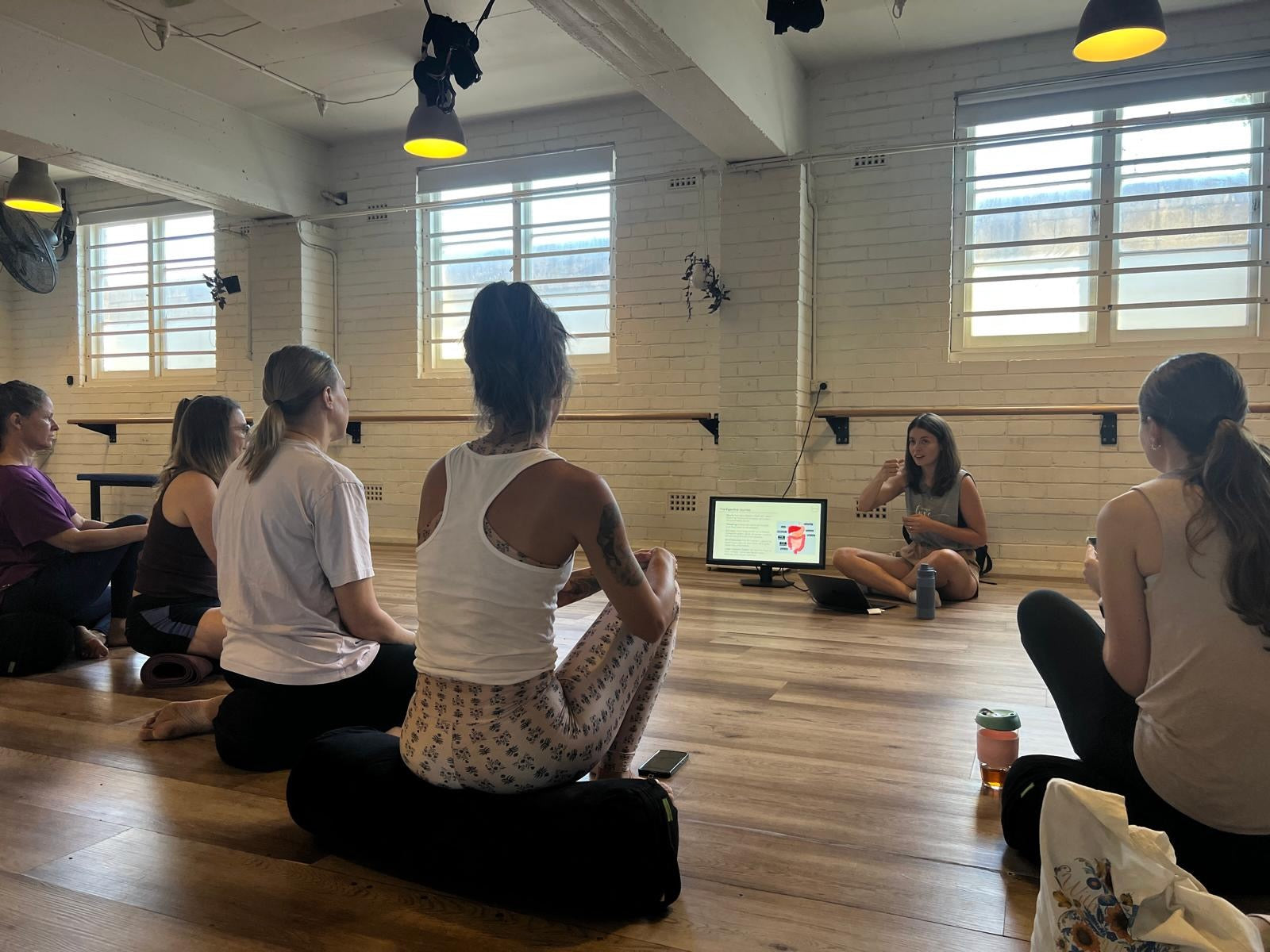 Group of people in a yoga studio with a screen displaying content and Nuala presenting.